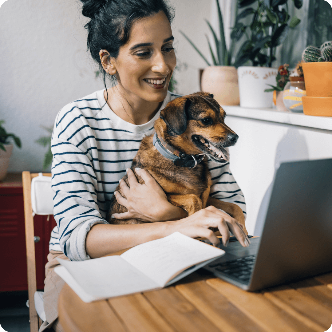 Woman on computer smiling holding brown dog